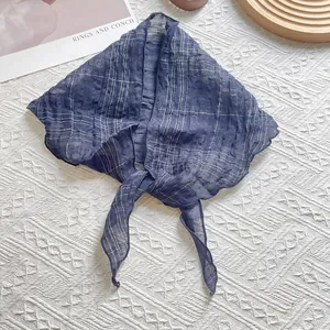 Détail d'un foulard en lin bleu marine à carreaux avec bords ondulés sur fond texturé