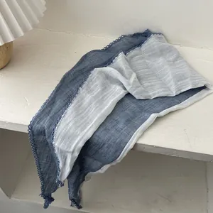 Détail d'une écharpe en coton et lin bicolore avec bordure en dentelle sur bois blanc