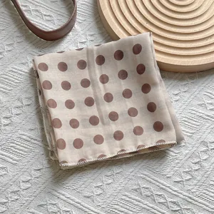 Vintage beige polka dot silk scarf for women styled on a minimalist wooden base