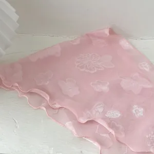 Detail eines rosa Gazeschals mit weißem Blumenjacquard und zarten Rüschenrändern