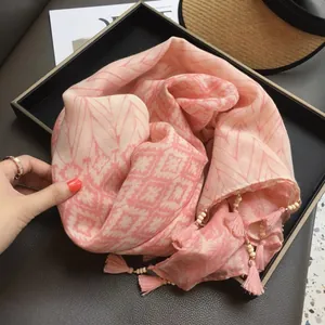 Détail d'un châle rose à motif ethnique avec pompons et perles blanches