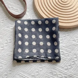 Detailed view of lightweight black silk scarf with white polka dots on textured surface