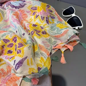 Détail d'une écharpe à motifs de feuilles colorées avec glands et lunettes de soleil