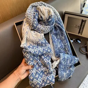 Détail du motif plume bleu sur écharpe en coton blanc avec bordure à pompons fins