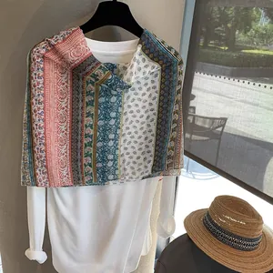Detail of bohemian floral print scarf with tassels layered over white top and sun hat