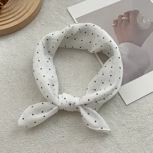 Classic white silk scarf with black polka dots styled on a wooden tray with decor