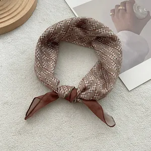 Dettaglio di un foulard di seta marrone con motivo pied de poule annodato ad anello