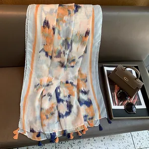 Detail of light gradient ink print scarf with orange and blue fringe on a leather sofa