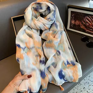 Detailed view of the gradient ink art scarf with orange tassels on a gray background