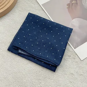 Macro view of navy blue polka dot silk scarf with delicate hemmed edges on soft fabric