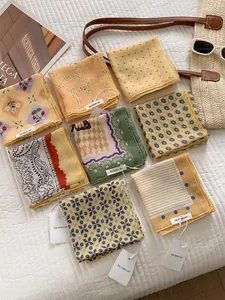 Flat lay of multiple floral cotton linen small square scarves with summer styling accessories