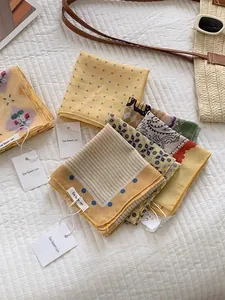Detail of assorted summer silk scarves with floral patterns, tags, and beach accessories