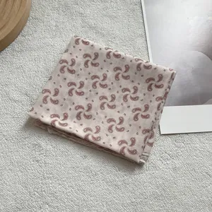 Beige silk scarf with paisley patterns displayed on a soft textured background