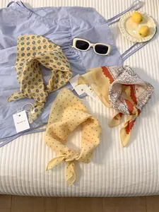 Three elegant scarves with floral, polka dot, and paisley prints on a white bedsheet
