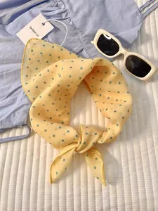 Detail of yellow polka dot neck scarf tied on a light blue summer dress with sunglasses