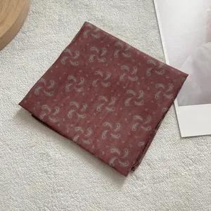 Macro detail of red paisley printed silk scarf showing fine edge stitching and texture
