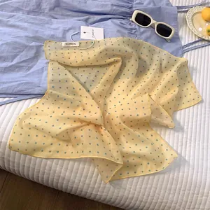 Detailed texture of lightweight yellow chiffon scarf with blue polka dots and hemmed edges