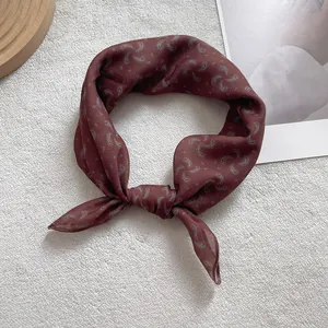 Detail view of burgundy paisley silk scarf on plush background with decorative props