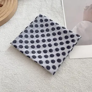 Detail of grey cotton scarf with black brush-stroke polka dots on wooden tray