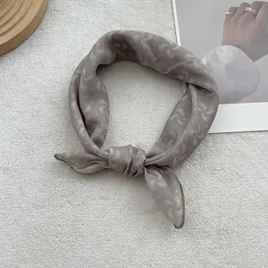 Close-up of taupe silk scarf with paisley pattern tied in a knot on white texture