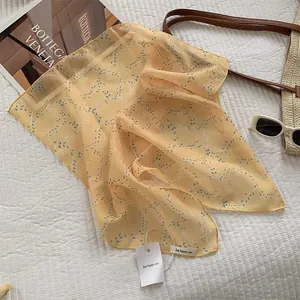 Detail view of yellow linen-silk scarf with green leaf pattern and white paper hangtag