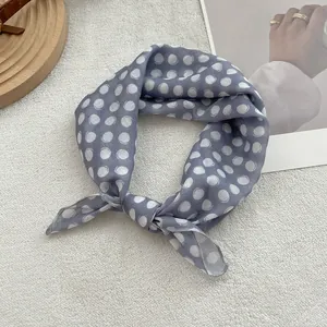 Detail of grey-blue polka dot silk scarf tied on a minimalist magazine background