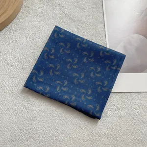 Close-up of navy blue paisley silk scarf with gold patterns on a minimalist wood tray
