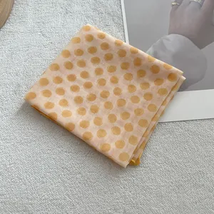 Macro detail of sunset yellow polka dot cotton linen scarf on white plush background