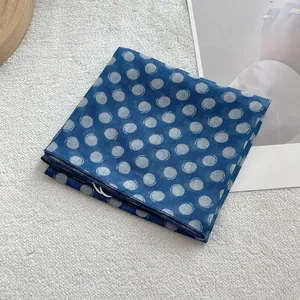 Detailed shot of blue linen silk scarf with white spiral polka dots on a texture mat