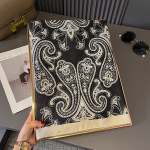 Elegant black and white paisley silk scarf with gold border displayed with accessories