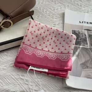 Detailed view of pink polka dot silk scarf with lace print and brand tag on knit surface