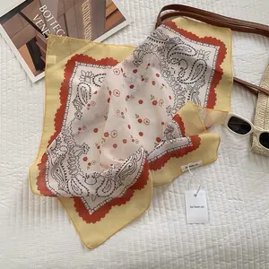 Flat lay of yellow paisley square scarf with summer sunglasses and woven bag on white quilt