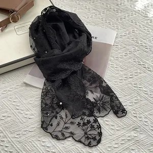 Detail of black floral lace scarf with embroidery and pearl accents on textured ground