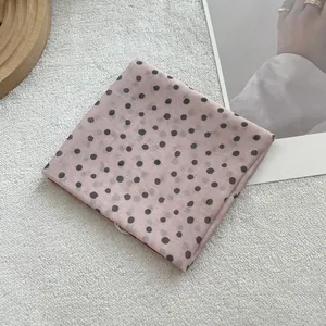 Detailed close-up of soft pink polka dot scarf on a wooden tray and white plush surface