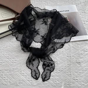 Détail d'un foulard en dentelle noire avec broderies florales sur fond de tissu blanc