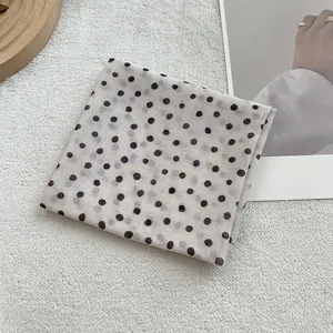 Detail of soft white cotton-linen scarf with black polka dots on an aesthetic surface