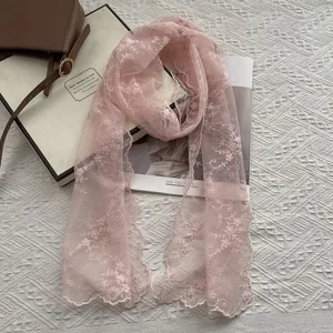 Detailed view of floral embroidery and scalloped edges on a pale pink lace scarf