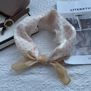 Close-up of a floral polka dot square scarf styled with a leather bag and magazine
