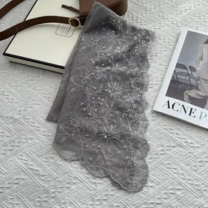 Detail of grey lace scarf with floral embroidery, pearls and sequins on white background