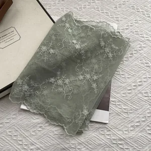 Detail of light green mesh scarf with white floral embroidery and wavy lace edges
