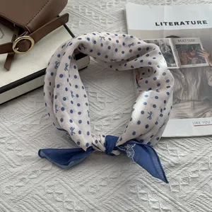 Close-up of a cream and blue polka dot silk scarf with bow patterns on a textured background