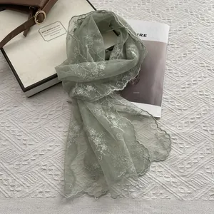 Close-up of light green mesh scarf with white floral embroidery and wavy hem details