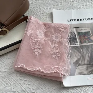 Detail of pink lace scarf with floral embroidery and scalloped edges on white fabric
