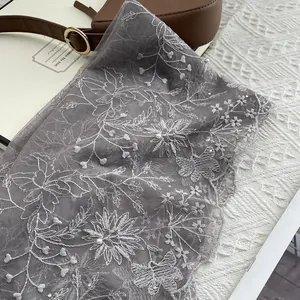 Detail of grey lace scarf featuring delicate white floral embroidery and pearl accents
