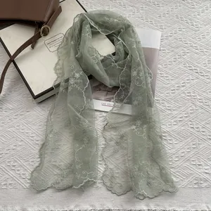 Close-up of sage green lace scarf featuring delicate floral embroidery and scalloped edges