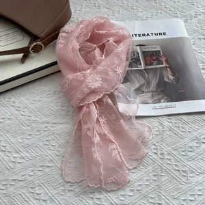 Detail of pink lace scarf with floral embroidery beside a book and leather bag