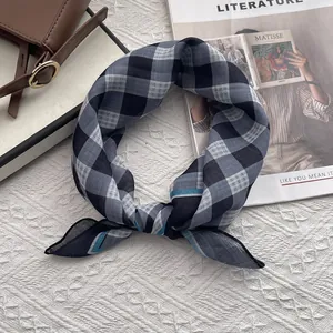 Dettaglio di un foulard in cotone a quadretti blu e grigi annodato accanto a borsa e rivista