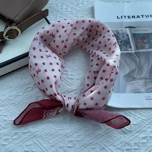 Close-up of pink polka dot silk scarf with bow pattern on a soft textured surface