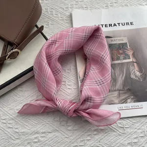 Dettaglio di un foulard in cotone a quadretti rosa annodato su sfondo bianco materico