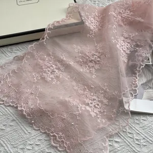 Detail of pink lace scarf with floral embroidery, pearls, and rhinestones on white backdrop